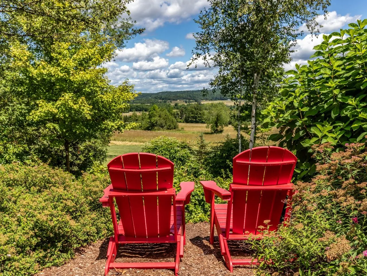 Two red Adirondack chairs overlooking farmland